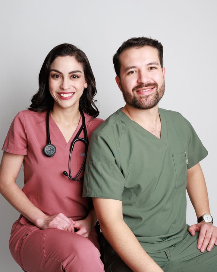 La Dra. Mariana Macías y el Dr. Ramsés Zúñiga, pediatras intensivistas en Chihuahua, sonriendo en uniforme quirúrgico con estetoscopio.